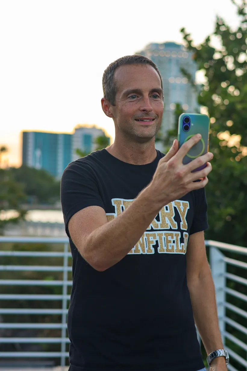 Jerry Banfield holding up a phone with the St. Petersburg, Florida skyline behind him